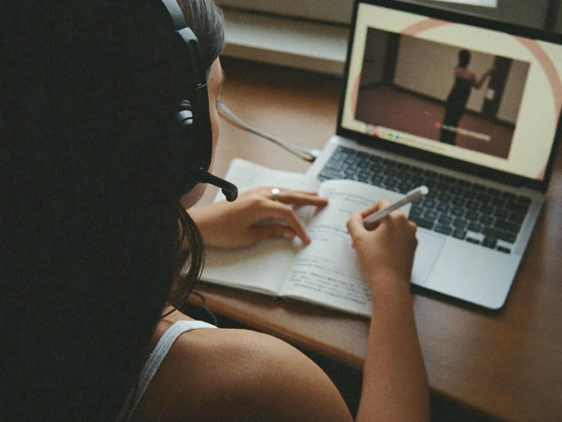A woman wearing a headset takes notes while a training video plays on her laptop